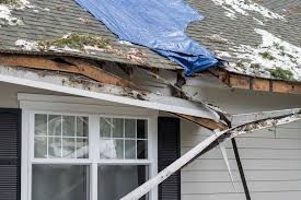 Storm-damaged roof with a tarp covering torn shingles and exposed decking after heavy rain